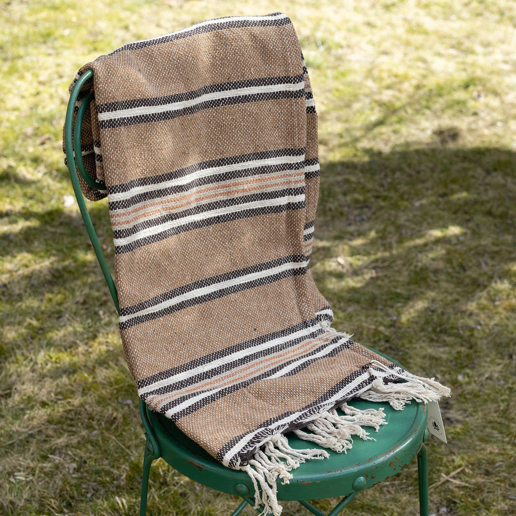 Striped, brown blanket draped over a green chair on grass