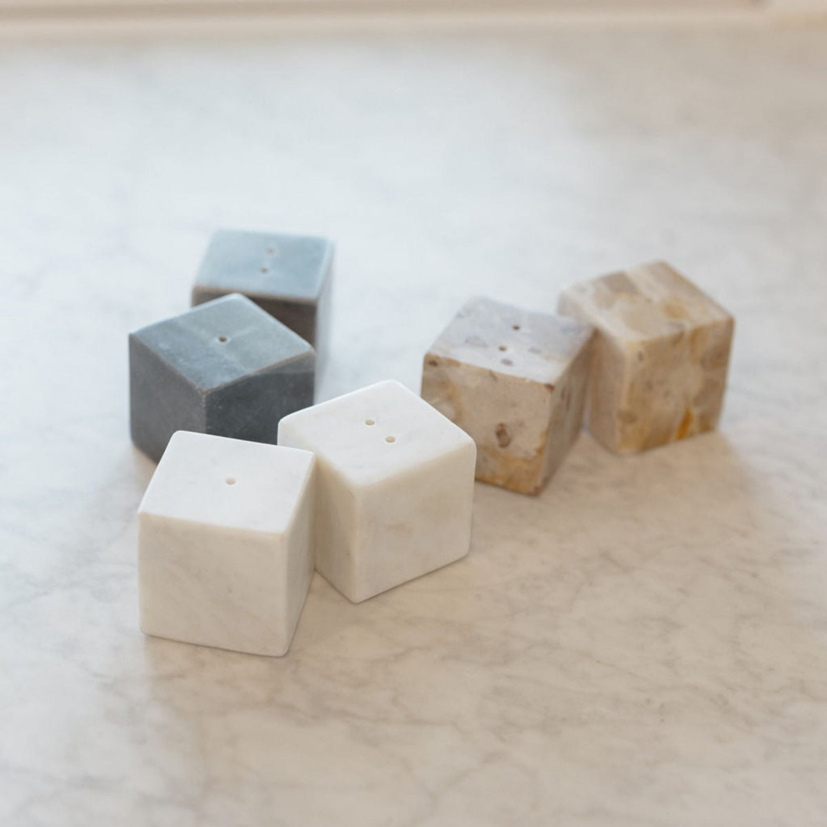 A set of marble salt and pepper shakers in various colors including black, natural, and white, displayed on a marble surface.