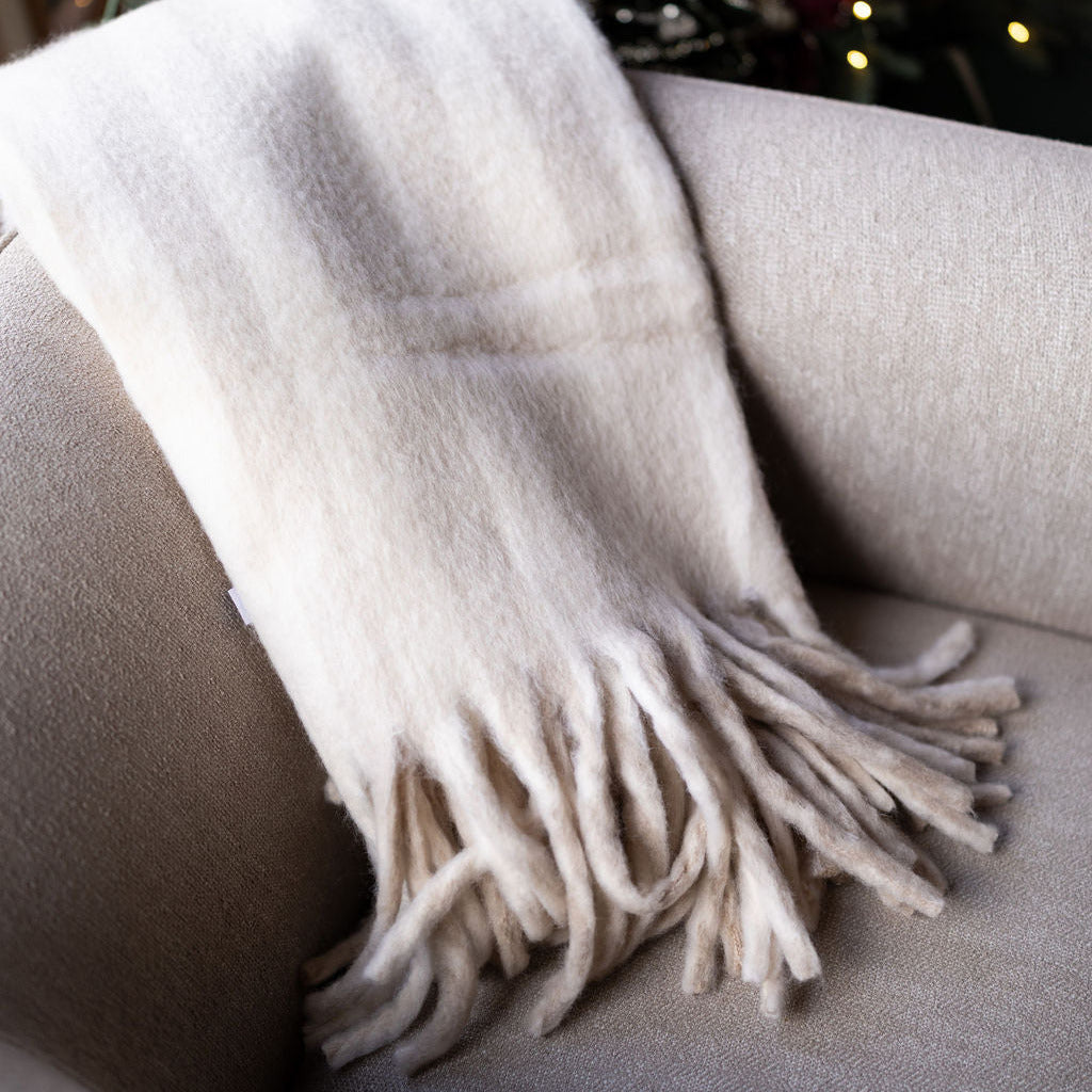 Pale beige striped, cozy blanket with tassels on beige chair