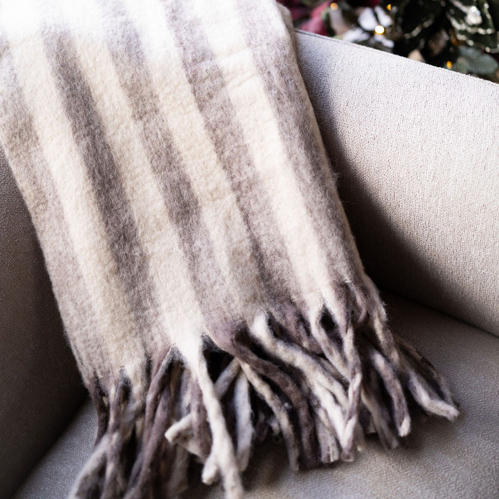 Brown and beige striped, cozy blanket with tassels on beige chair